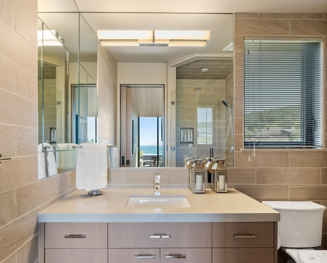 full bathroom featuring toilet, vanity, tiled shower, and tile walls