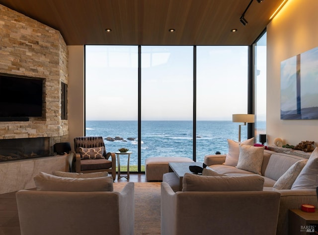 living room featuring expansive windows, a water view, wooden ceiling, and a stone fireplace