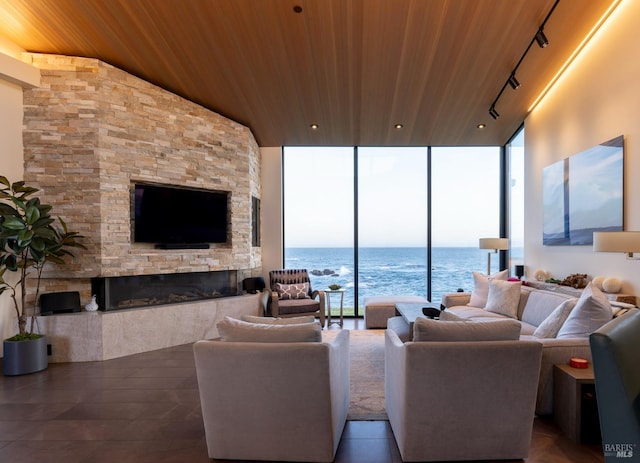 living area featuring track lighting, wood ceiling, a stone fireplace, and expansive windows