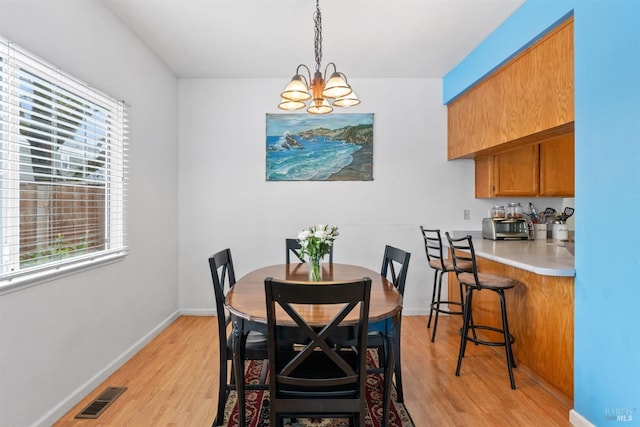 dining space with light wood-style flooring, a notable chandelier, baseboards, and visible vents