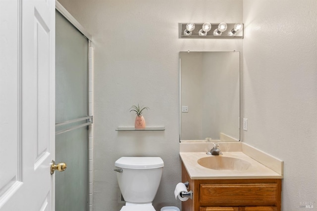 bathroom featuring a shower with door, toilet, and vanity