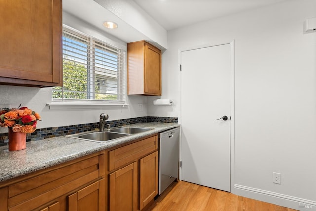 kitchen with light wood finished floors, brown cabinets, stainless steel dishwasher, and a sink