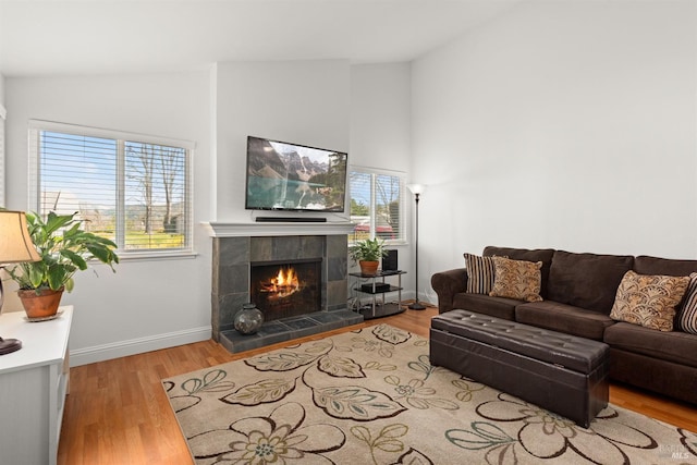 living room featuring vaulted ceiling, wood finished floors, baseboards, and a tile fireplace