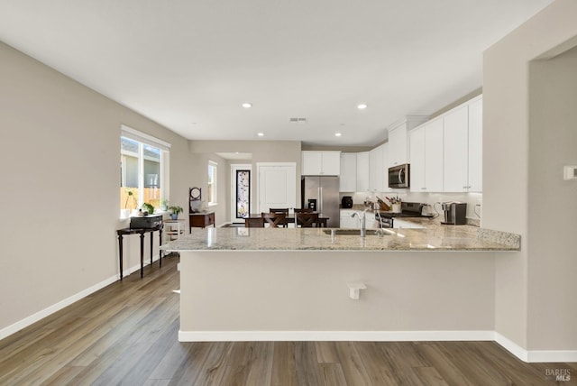 kitchen featuring baseboards, light stone countertops, a peninsula, stainless steel appliances, and a sink