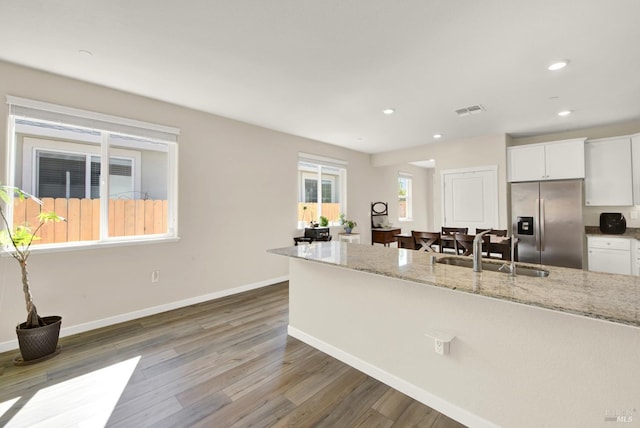 kitchen featuring light stone countertops, visible vents, stainless steel fridge with ice dispenser, a sink, and white cabinets