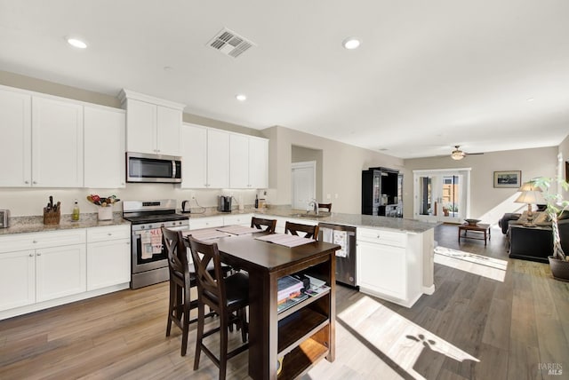 kitchen featuring visible vents, open floor plan, a peninsula, stainless steel appliances, and a sink