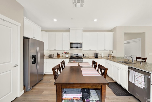 kitchen with visible vents, light wood finished floors, a sink, stainless steel appliances, and white cabinets