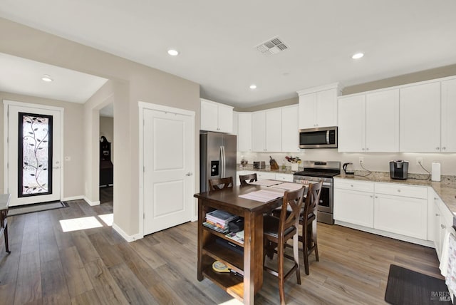 kitchen featuring light stone counters, visible vents, appliances with stainless steel finishes, and wood finished floors