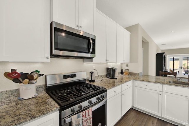 kitchen featuring light stone counters, a sink, dark wood-type flooring, appliances with stainless steel finishes, and white cabinetry