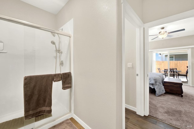 ensuite bathroom with a shower stall, wood finished floors, baseboards, and ceiling fan