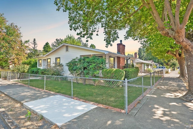 ranch-style house with a front lawn, a fenced front yard, a chimney, driveway, and a gate