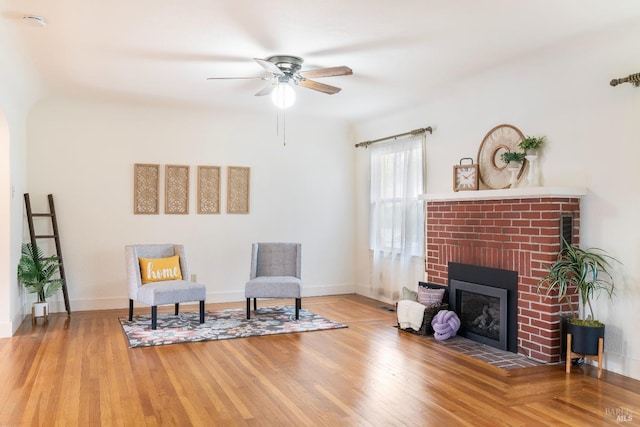 sitting room with baseboards, a fireplace, wood finished floors, and a ceiling fan