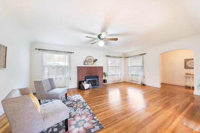 living room with a ceiling fan, baseboards, a fireplace, arched walkways, and light wood-type flooring