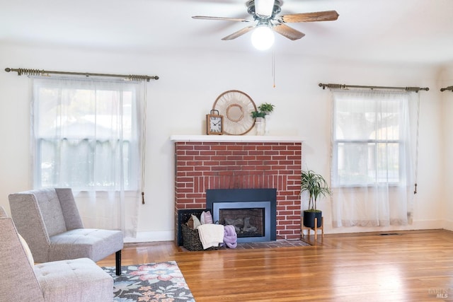 living area featuring a fireplace, wood finished floors, a healthy amount of sunlight, and ceiling fan