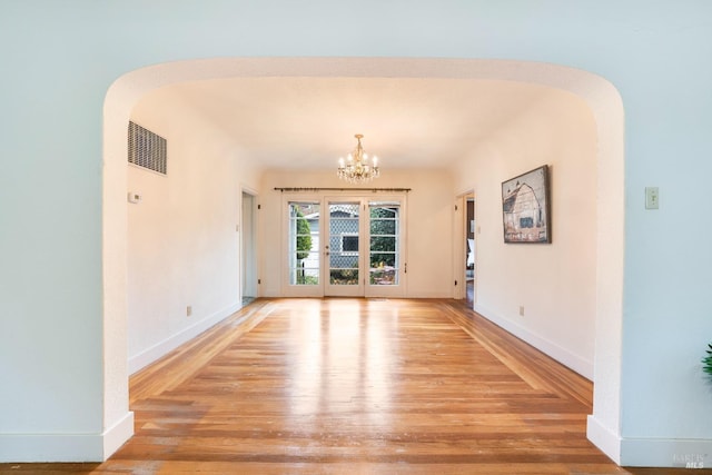 empty room with visible vents, arched walkways, light wood finished floors, baseboards, and a chandelier