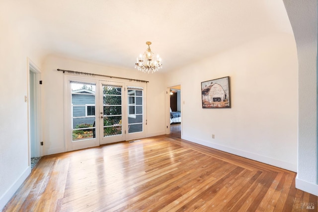 spare room featuring visible vents, light wood-style flooring, baseboards, and an inviting chandelier