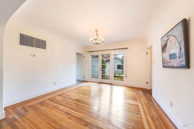 spare room featuring a notable chandelier, light wood-style floors, visible vents, and baseboards