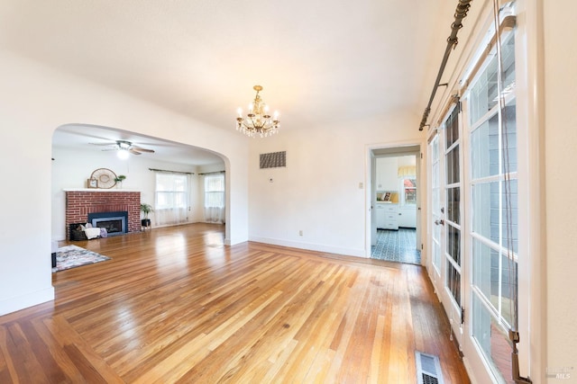 unfurnished living room featuring visible vents, a fireplace, arched walkways, ceiling fan with notable chandelier, and light wood-type flooring