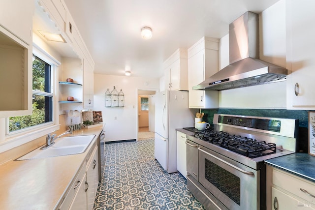 kitchen with wall chimney range hood, stainless steel range with gas stovetop, dishwasher, freestanding refrigerator, and a sink