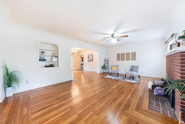 living area with baseboards, arched walkways, a brick fireplace, and ceiling fan with notable chandelier