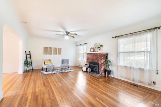 living area with wood finished floors, baseboards, visible vents, a fireplace, and ceiling fan