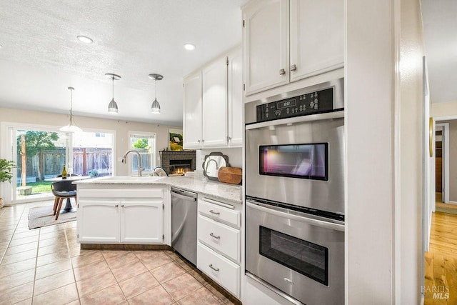 kitchen featuring a peninsula, a fireplace, a sink, stainless steel appliances, and white cabinets