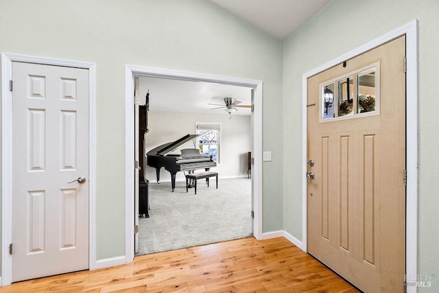 foyer featuring light wood-type flooring, baseboards, light colored carpet, and a ceiling fan