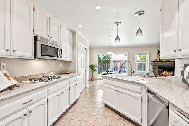 kitchen featuring a fireplace, white cabinets, a textured ceiling, stainless steel appliances, and a sink