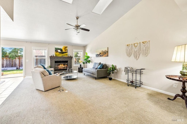 carpeted living area with a brick fireplace, baseboards, ceiling fan, a skylight, and high vaulted ceiling