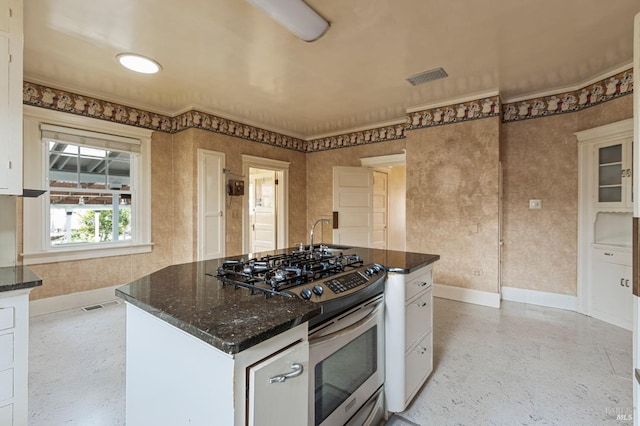 kitchen featuring dark stone counters, white cabinets, baseboards, and stainless steel gas stove