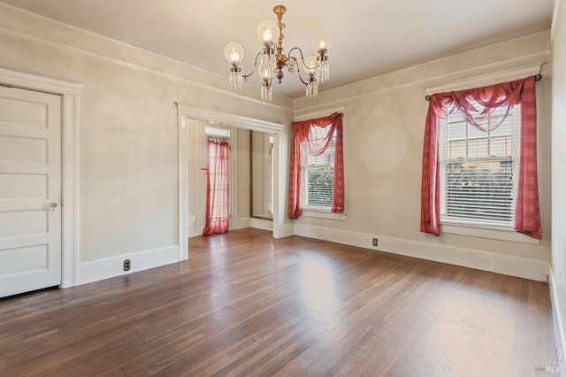 empty room with a chandelier, baseboards, and wood finished floors