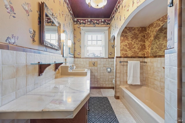 full bath featuring wallpapered walls, a tub, a wainscoted wall, and tile patterned flooring