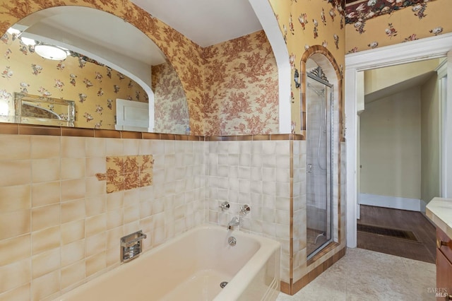 bathroom featuring a shower stall, a bath, wainscoting, and wallpapered walls