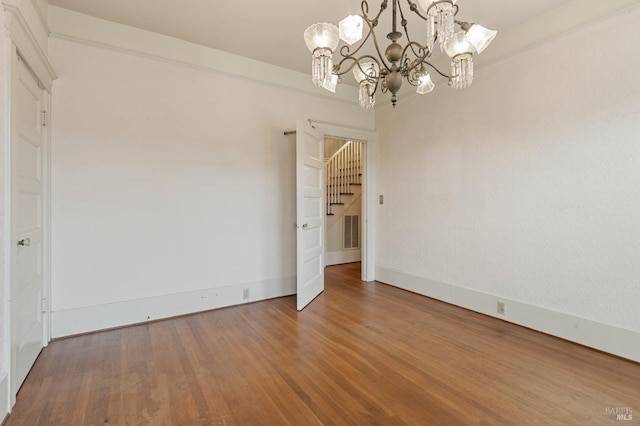 unfurnished room with visible vents, baseboards, an inviting chandelier, and wood finished floors