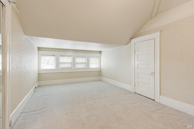 carpeted spare room featuring baseboards, lofted ceiling, and a textured wall