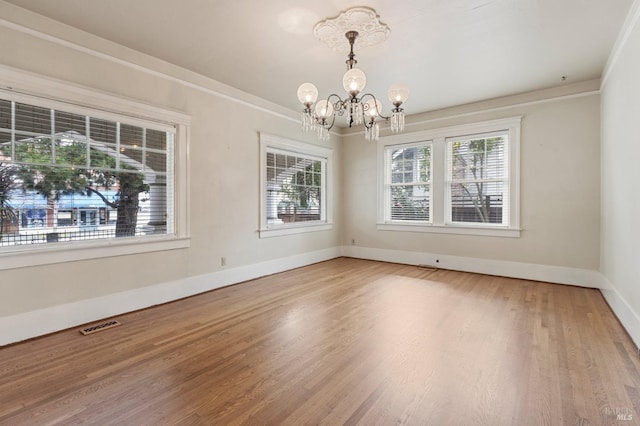 spare room featuring visible vents, baseboards, an inviting chandelier, ornamental molding, and light wood-type flooring