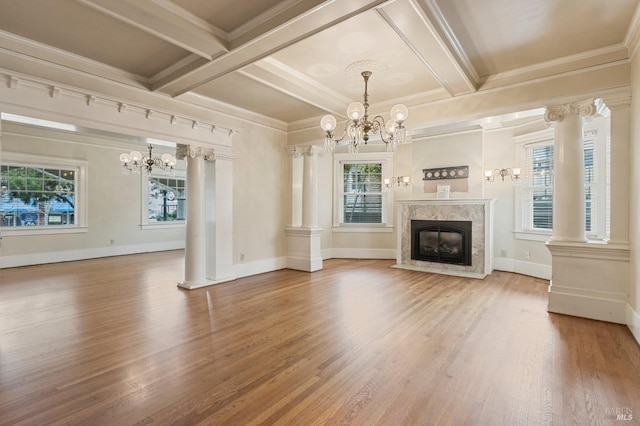 unfurnished living room with a chandelier, a healthy amount of sunlight, and decorative columns