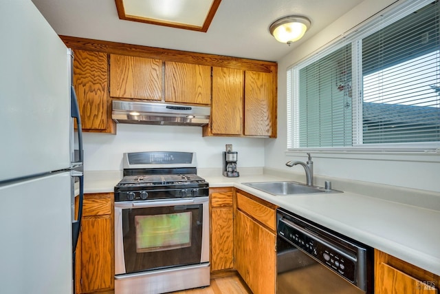 kitchen featuring stainless steel range with gas cooktop, under cabinet range hood, black dishwasher, freestanding refrigerator, and a sink