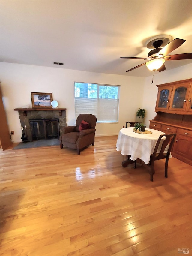 dining space with a glass covered fireplace, a ceiling fan, visible vents, and light wood-type flooring