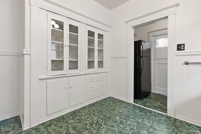 interior space featuring a wainscoted wall, glass insert cabinets, white cabinets, and freestanding refrigerator