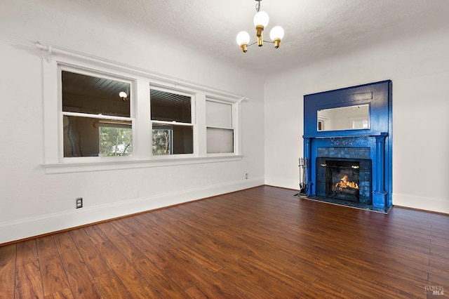 unfurnished living room featuring a chandelier, a tile fireplace, baseboards, and dark wood-style flooring