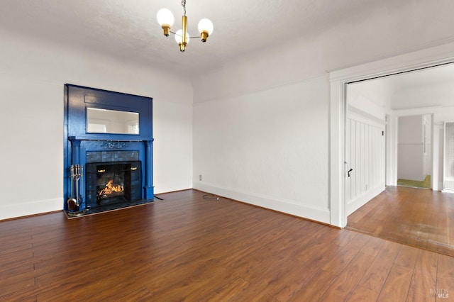 unfurnished living room with baseboards, wood-type flooring, a chandelier, and a tiled fireplace