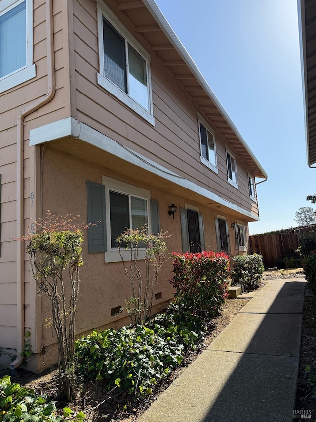 view of side of property with crawl space, stucco siding, and fence