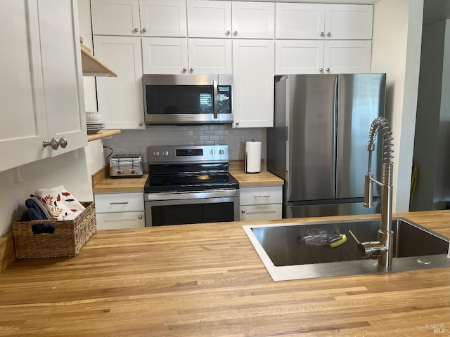 kitchen featuring stainless steel appliances, backsplash, white cabinets, and butcher block counters