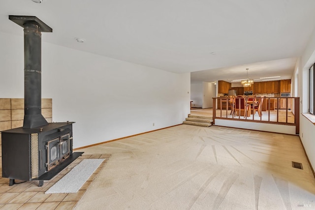 living area with visible vents, light carpet, an inviting chandelier, baseboards, and a wood stove