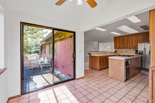 kitchen featuring ceiling fan, stainless steel fridge with ice dispenser, decorative backsplash, a peninsula, and gas cooktop