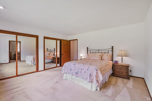 bedroom featuring light carpet, baseboards, and multiple closets