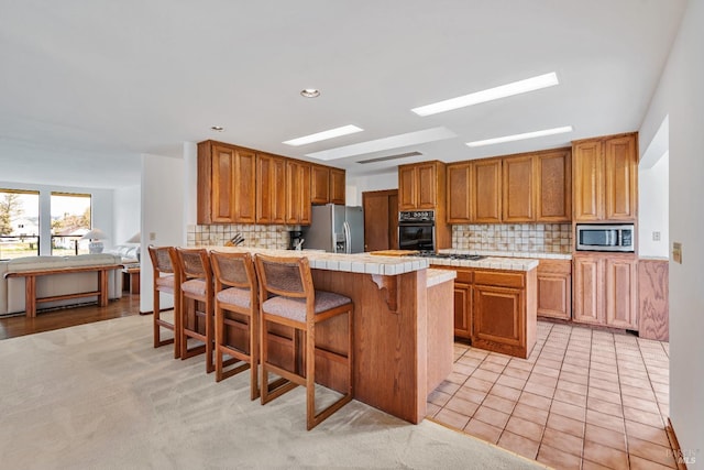 kitchen with a breakfast bar area, a peninsula, stainless steel appliances, tile counters, and brown cabinets