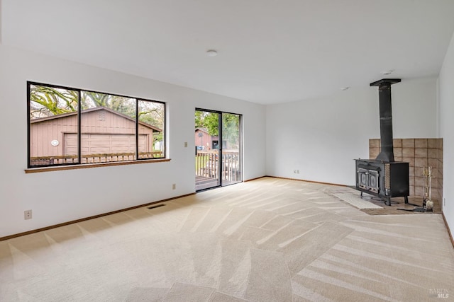 unfurnished living room featuring a wood stove, baseboards, and carpet floors