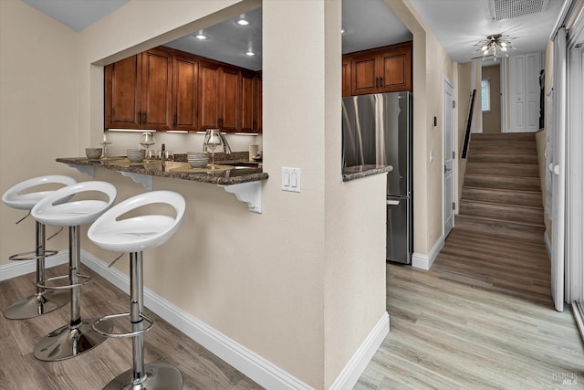 kitchen featuring a kitchen bar, visible vents, light wood finished floors, and freestanding refrigerator